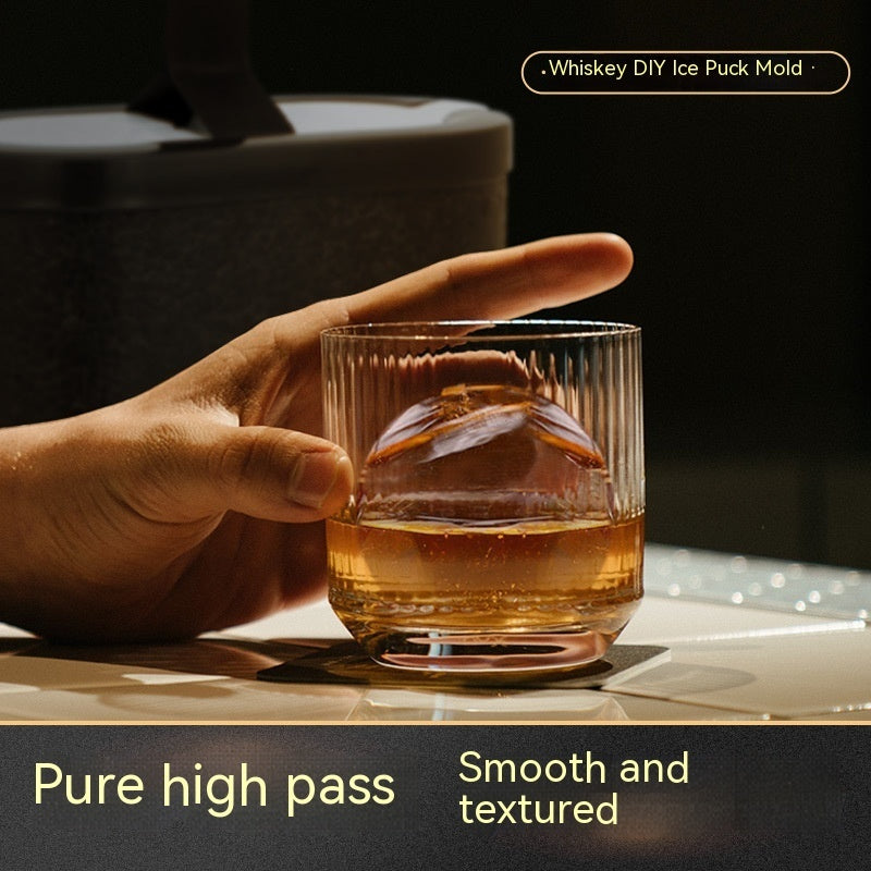 Hand holding a whiskey glass with a large clear ice sphere, made using a DIY ice puck mold.